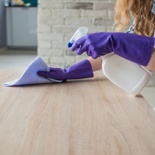 A professional cleaner spraying cleaner and wiping down a wooden surface.