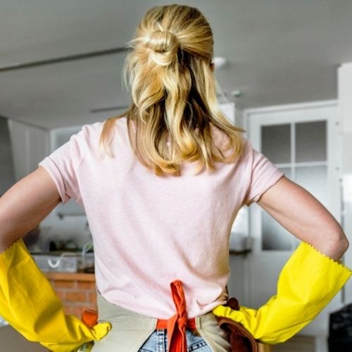 A woman wearing yellow rubber gloves stands facing away from the camera with her hands on her hips.