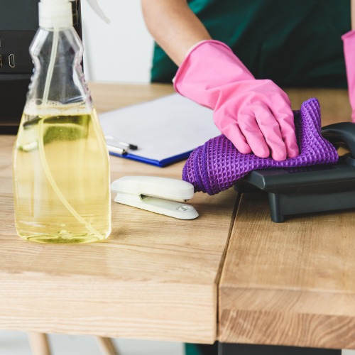 A professional office cleaner sanitizing a desktop phone.