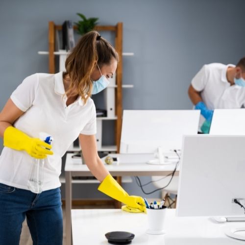A commercial cleaning technician disinfecting a desk in an office.