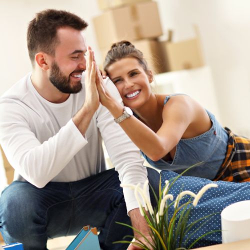 A happy man and woman high-fiving surrounded by cardboard moving boxes.