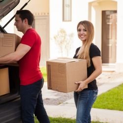 A man and woman loading cardboard moving boxes into the trunk of their vehicle.