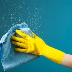 A person wearing yellow rubber gloves wiping a wet glass surface.