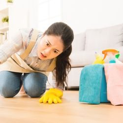 A maid looking distressed as she inspects a hardwood floor.